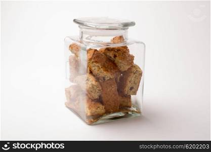 A square glass jar filled with rusks and lid on top on a white background.