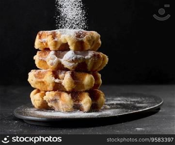 A stack of baked Belgian waffles sprinkled with powdered sugar