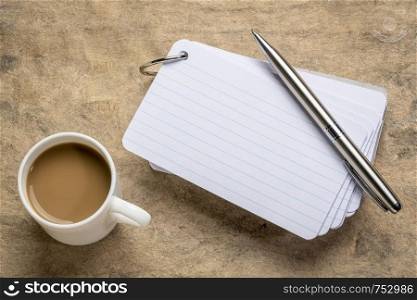a stack of blank index cards with a cup of coffee and a pen against textured bark paper