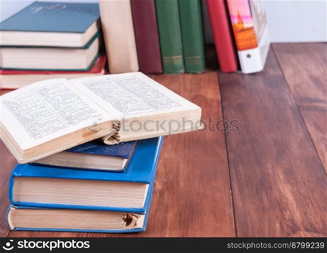 A stack of books with an open book lying on top. Books in stacks on the table in the background