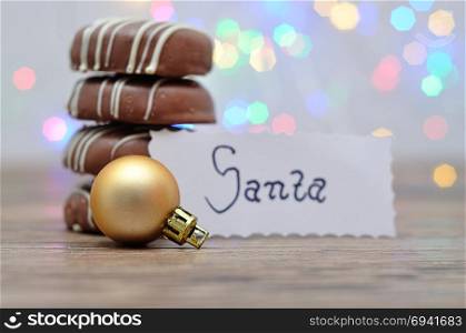 A stack of chocolate covered biscuits and a golden babble with a note for Santa