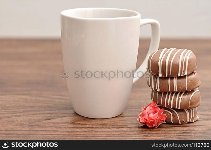 A stack of chocolate covered biscuits with an artificial rose and a white mug