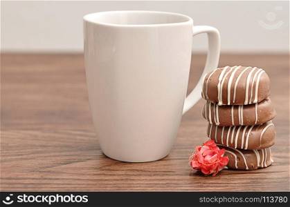 A stack of chocolate covered biscuits with an artificial rose and a white mug