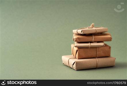 A stack of Christmas presents wrapped in ecological recycled paper on green background with copy space