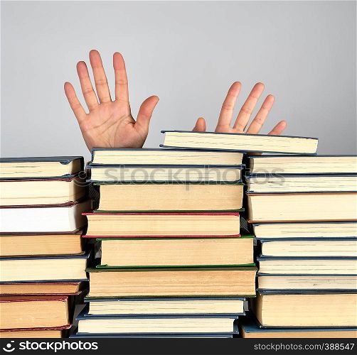a stack of different books on a gray background, two female hands stick out from behind a heap, concept of learning