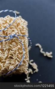 A stack of homemade instant noodles rewound with a blue rope on a black background.. A stack of homemade instant noodles rewound with a blue rope on a black background
