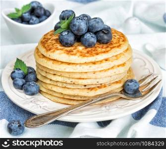 A stack of pancakes decorated with ripe berries of blueberries on the background of blue-white napkin