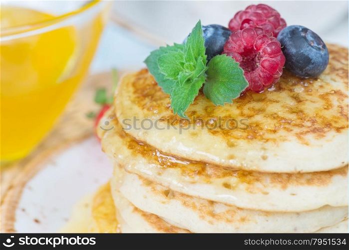 A stack of pancakes decorated with ripe raspberries and blueberries close-up