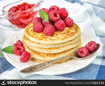 A stack of pancakes decorated with ripe raspberries and sauceboat with jam in the background
