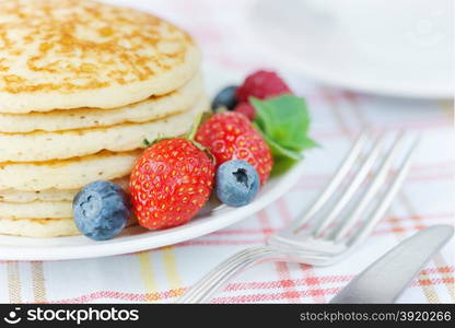 A stack of pancakes decorated with ripe strawberry and blueberries close-up