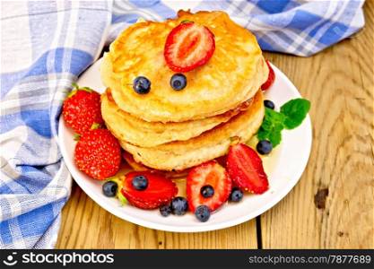 A stack of pancakes with strawberries, blueberries and honey on a white plate, napkin on a wooden boards background