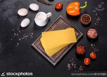 A stack of raw lasagna sheets with herbs and spices on a dark concrete background. Stack of lasagna sheets on a dark concrete background. Ingredients for lasagna