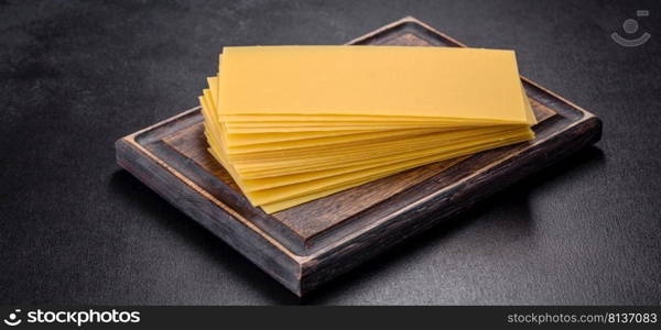 A stack of raw lasagna sheets with herbs and spices on a dark concrete background. Stack of lasagna sheets on a dark concrete background. Ingredients for lasagna