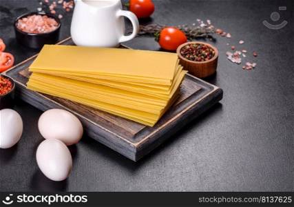A stack of raw lasagna sheets with herbs and spices on a dark concrete background. Stack of lasagna sheets on a dark concrete background. Ingredients for lasagna