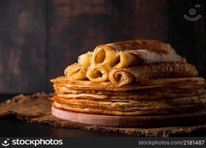 A stack of thin pancakes on a dark wooden background. A traditional dish of crepes for the holiday Maslenitsa. Place for your text, photo for design.. A stack of thin pancakes on a dark wooden background. A traditional dish of crepes for the holiday Maslenitsa.