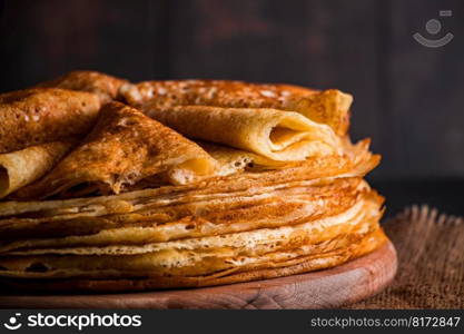 A stack of thin pancakes on a dark wooden background close up. A traditional dish of crepes for the holiday Maslenitsa. Place for your text, photo for design.. A stack of thin pancakes on a dark wooden background. A traditional dish of crepes for the holiday Maslenitsa.