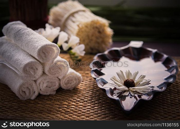 A stack of white towels and a container of water and a flower. Accessories for spa. A stack of white towels and a container of water and a flower.