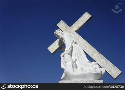 A statue of Jesus carrying the cross on blue sky background.