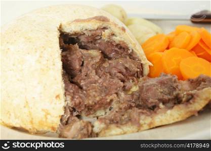A steak and kidney pudding cut open on a serving platter with carrots and potatoes and the knife in the background