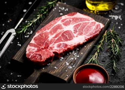 A steak of raw pork on a cutting board with tomato sauce and rosemary. On a black background. High quality photo. A steak of raw pork on a cutting board with tomato sauce and rosemary.