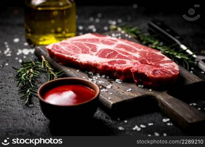 A steak of raw pork on a cutting board with tomato sauce and rosemary. On a black background. High quality photo. A steak of raw pork on a cutting board with tomato sauce and rosemary.
