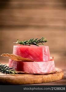 A steak of raw tuna on a cutting board with a sprig of rosemary. On a wooden background. High quality photo. A steak of raw tuna on a cutting board with a sprig of rosemary.