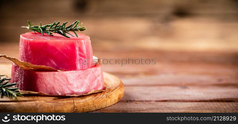 A steak of raw tuna on a cutting board with a sprig of rosemary. On a wooden background. High quality photo. A steak of raw tuna on a cutting board with a sprig of rosemary.