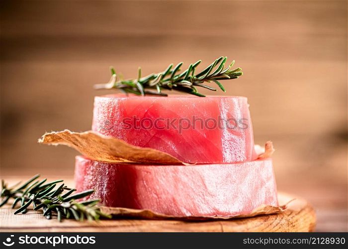 A steak of raw tuna on a cutting board with a sprig of rosemary. On a wooden background. High quality photo. A steak of raw tuna on a cutting board with a sprig of rosemary.