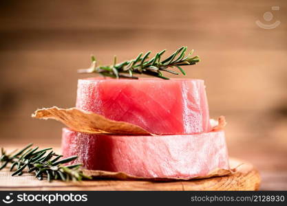 A steak of raw tuna on a cutting board with a sprig of rosemary. On a wooden background. High quality photo. A steak of raw tuna on a cutting board with a sprig of rosemary.