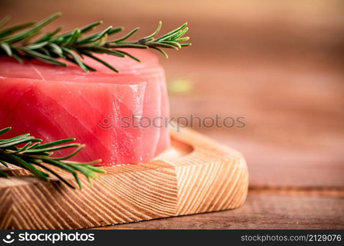 A steak of raw tuna on a cutting board with a sprig of rosemary. On a wooden background. High quality photo. A steak of raw tuna on a cutting board with a sprig of rosemary.