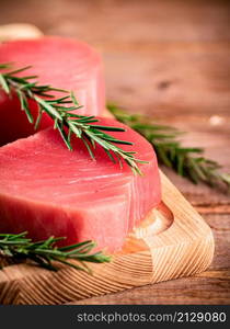 A steak of raw tuna on a cutting board with a sprig of rosemary. On a wooden background. High quality photo. A steak of raw tuna on a cutting board with a sprig of rosemary.