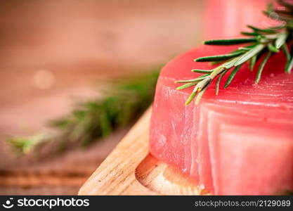 A steak of raw tuna on a cutting board with a sprig of rosemary. On a wooden background. High quality photo. A steak of raw tuna on a cutting board with a sprig of rosemary.