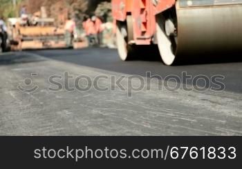 A steamroller rolls and compresses hot asphalt after it is spread by an asphalt paving machine