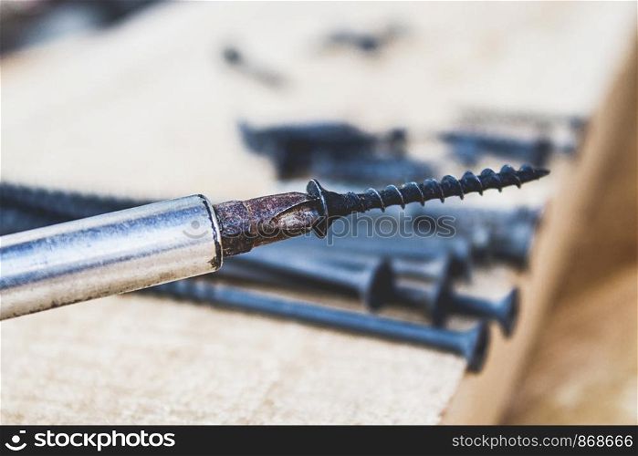 A steel screw is put on a screwdriver on a wooden board background. The concept of tools and repair work. Steel screws. Metal screw. A steel screw is put on a screwdriver on a wooden board background. The concept of tools and repair work. Steel screws.