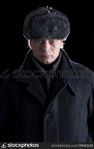 A stern looking man with a fur cap and a woolen coat looking straight into the camera