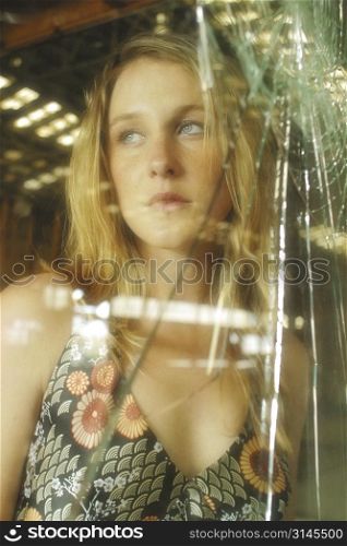 A stock photo of a woman looking scared through broken glass
