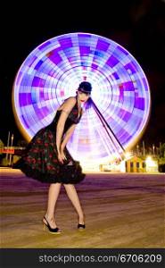 A stock photograph of a beautiful pin up model posing infront of a ferriswheel at night.