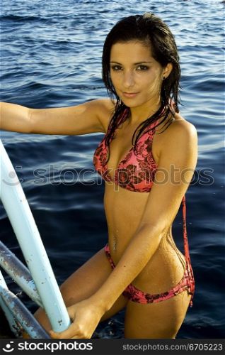 A stock photograph of a beautiful young woman posing on a ladder by the water in Malta.