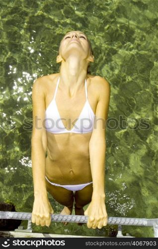 A stock photograph of a beautiful young woman relaxing in a white bikini by the water.