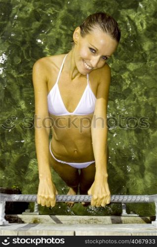 A stock photograph of a beautiful young woman relaxing in a white bikini by the water.