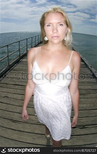 A stock photograph of a blonde woman relaxing by the beach in a white dress.