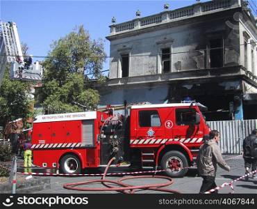 A stock photograph of a fire truck outside a burnt house.