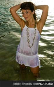 A stock photograph of a sexy young woman wearing a wet white dress in the water.