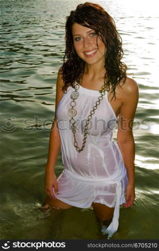 A stock photograph of a sexy young woman wearing a wet white dress in the water.