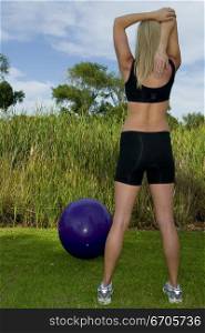 A stock photograph of a young woman exercising in the open air, stretching and being healthy.