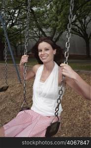 A stock photograph of a young woman sitting on a swing in a park.