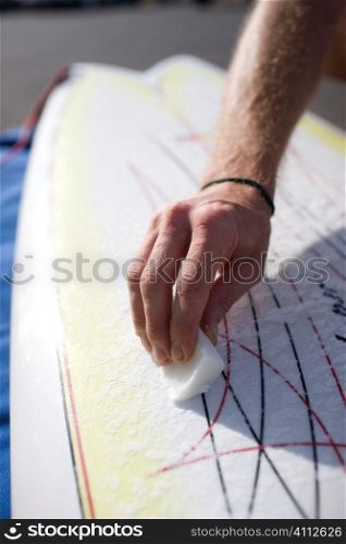 A stock photograph of man waxing his surfboard.