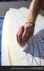 A stock photograph of man waxing his surfboard.