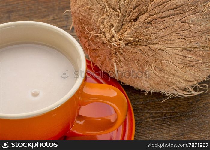 a stoneware cup of coconut milk with a coconut against wood background