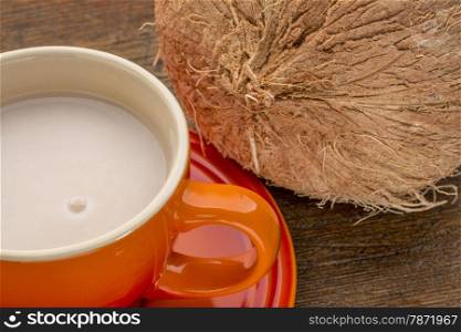 a stoneware cup of coconut milk with a coconut against wood background